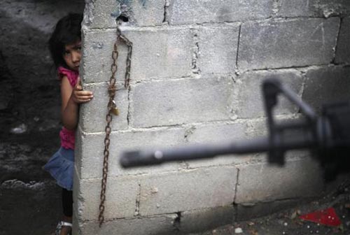 Bé gái sợ hãi đứng đằng sau một bước tường khi lực lượng cảnh sát đặt nhiệm vũ trang tiến hành tuần tra khu vực láng giềng thành phố Guadalupe, Mexico.